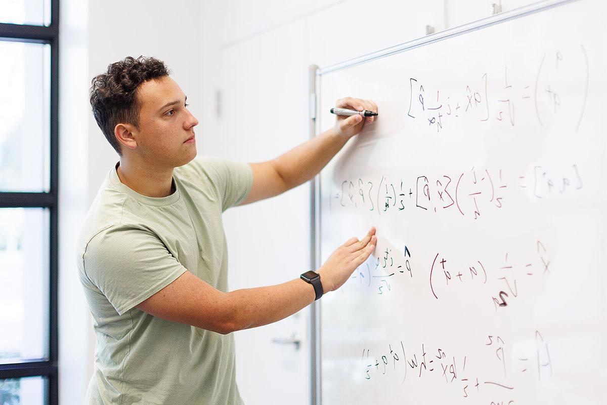 Student from engineering concentration in general engineering program writes equations on a whiteboard.